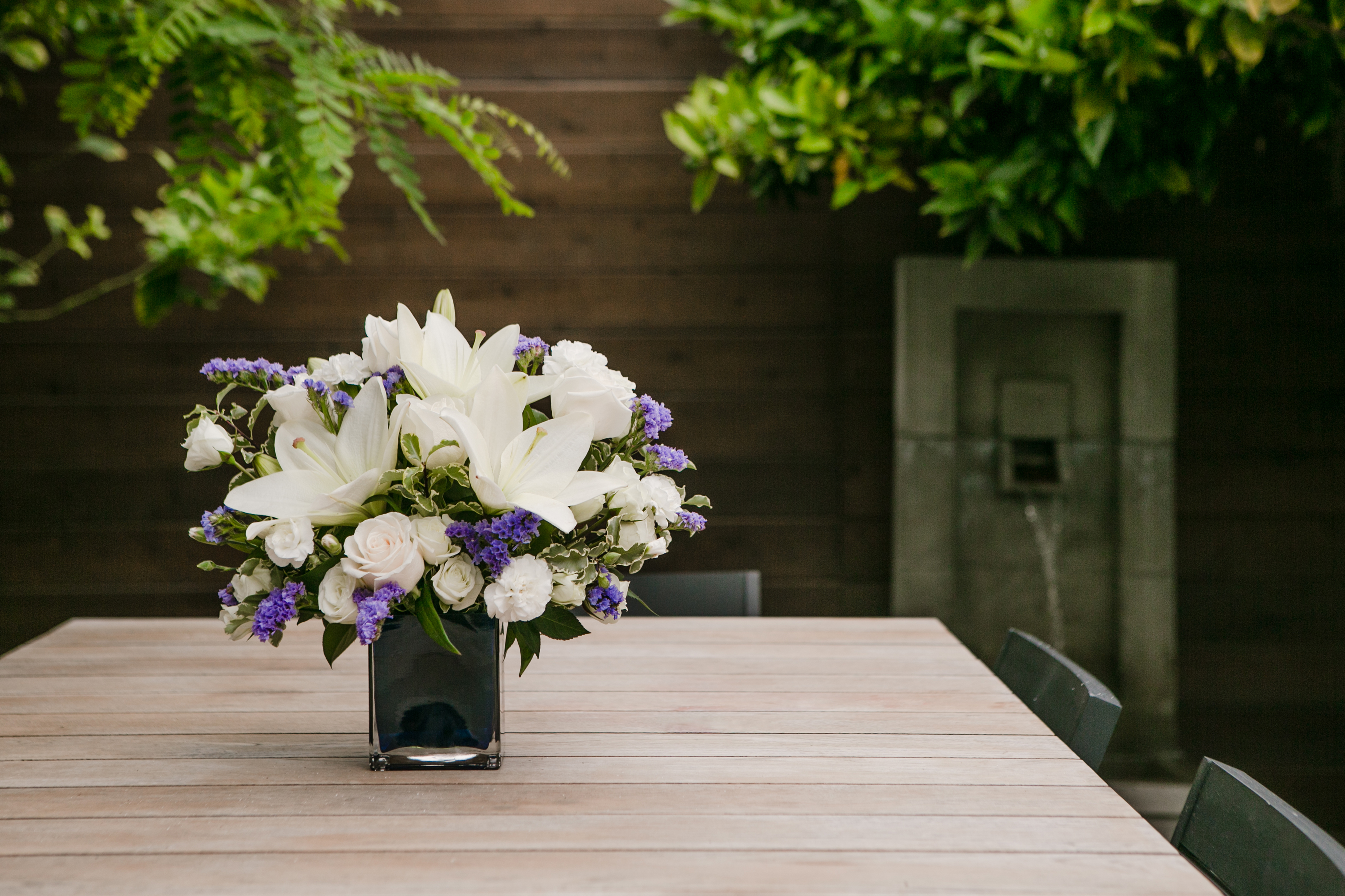 white roses, white lilies, and purple statice in a blue vase on a table