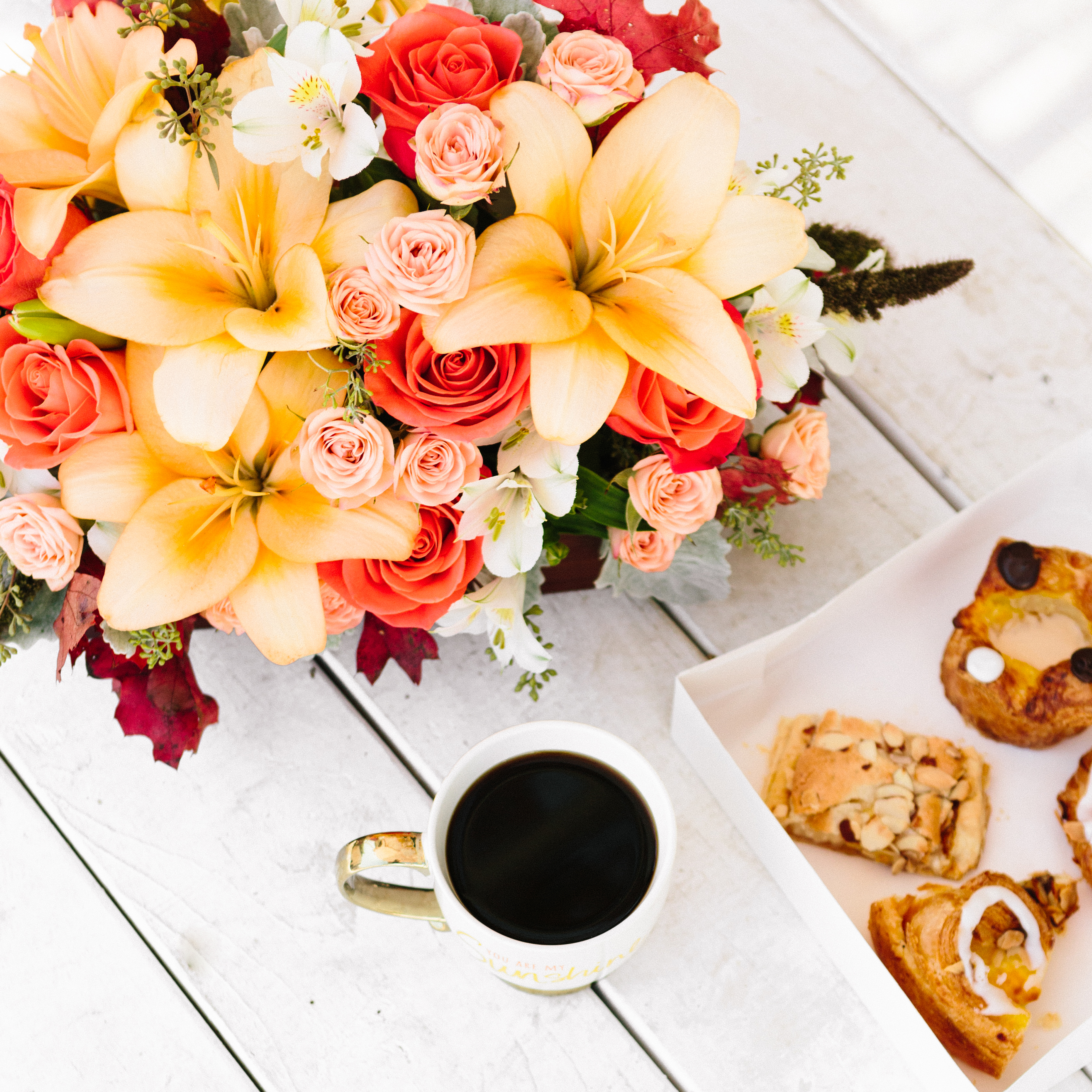 Orange lilies and roses on table with coffee and pastries