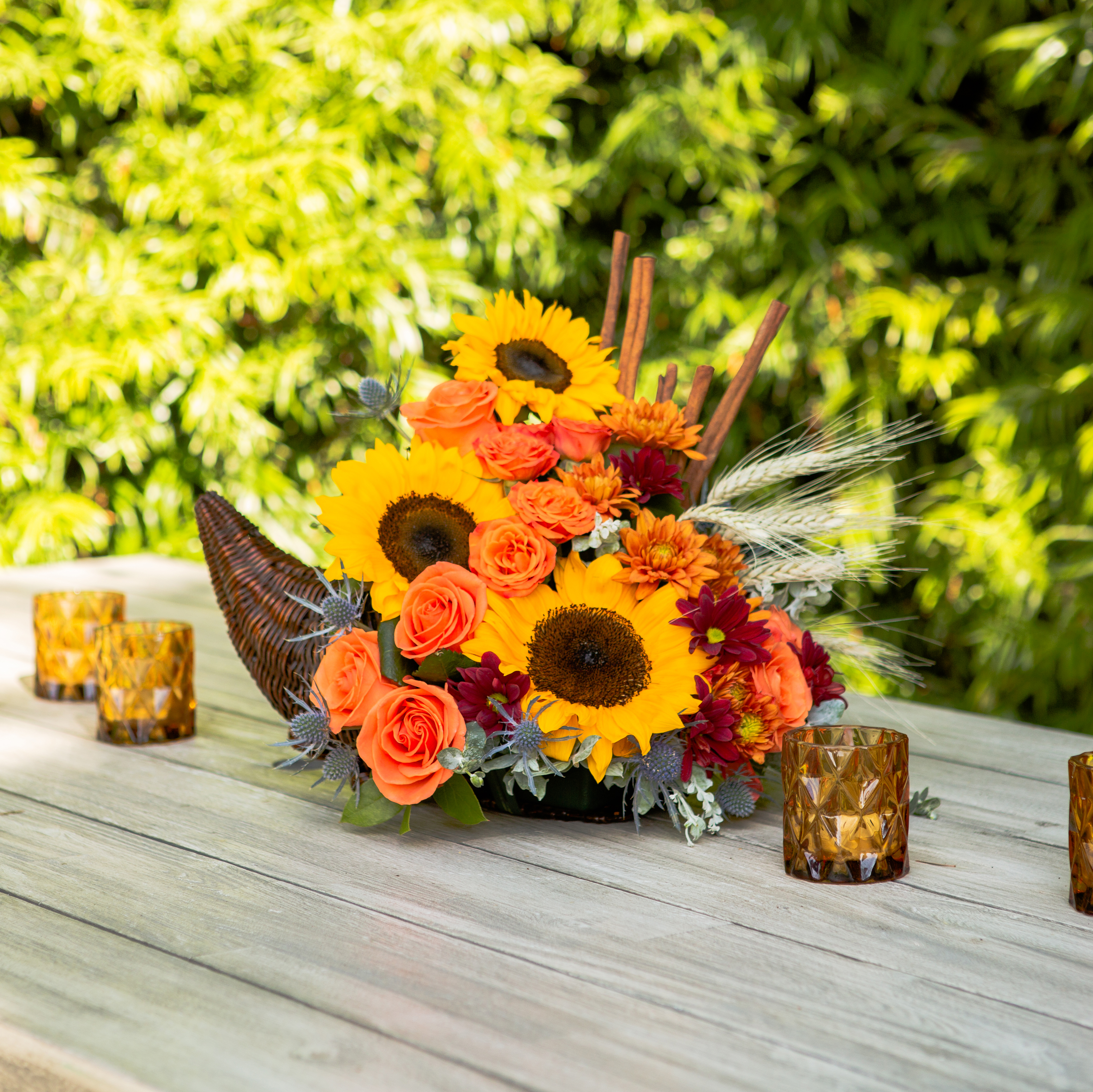 Sunflowers, orange roses, and more in wicker cornucopia on outdoor table
