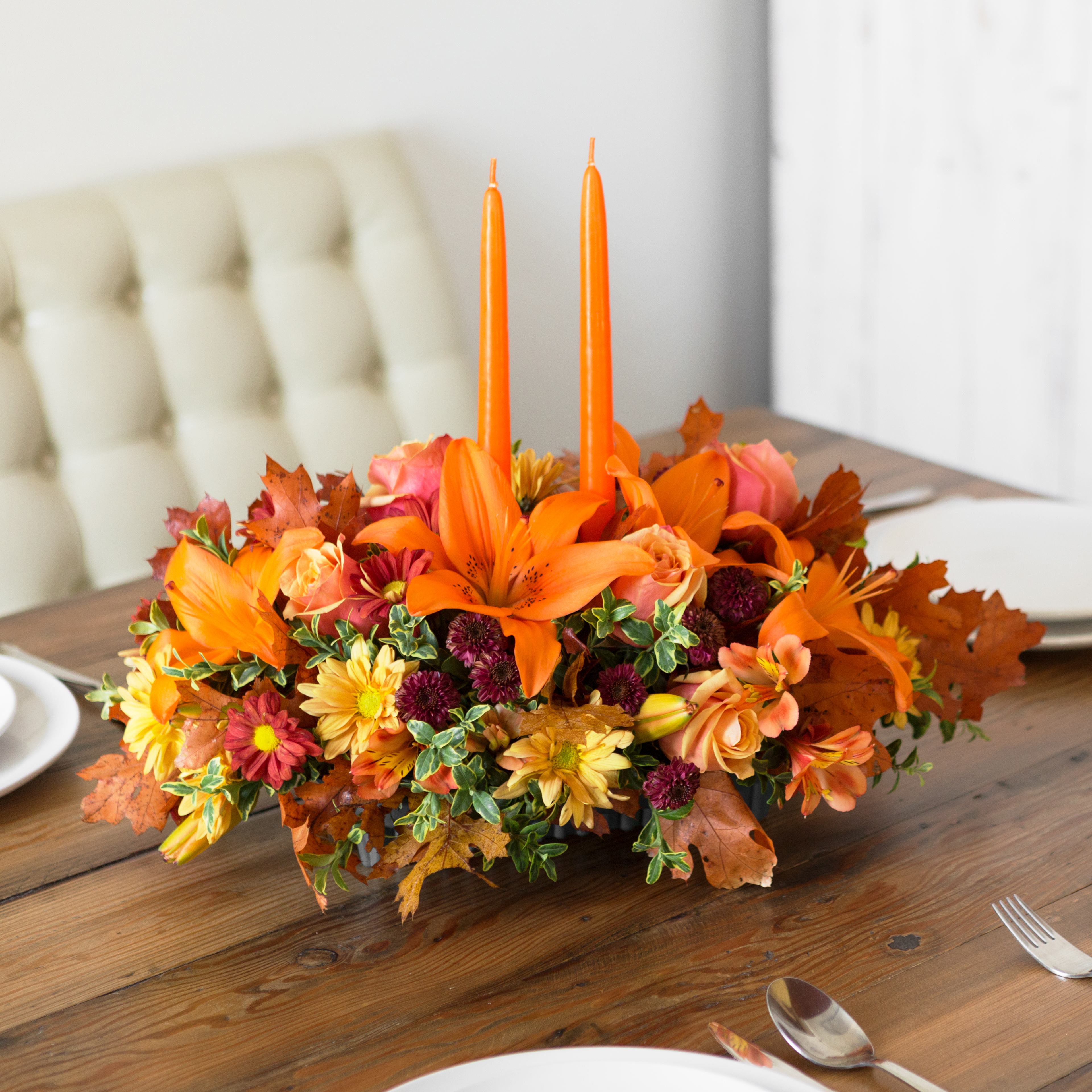 Orange lilies, purple mims, orange roses, and more in thanksgiving centerpiece with orange candles