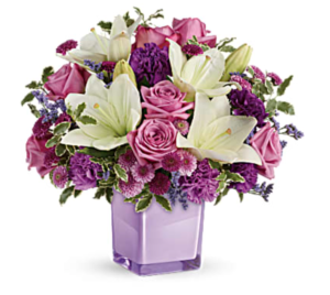 Purple roses and white lilies fill a purple cube vase