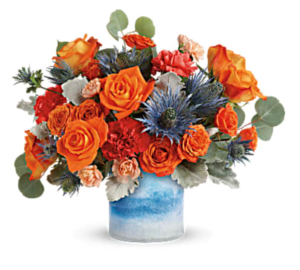 Orange roses and blue flowers fill a bright blue vase