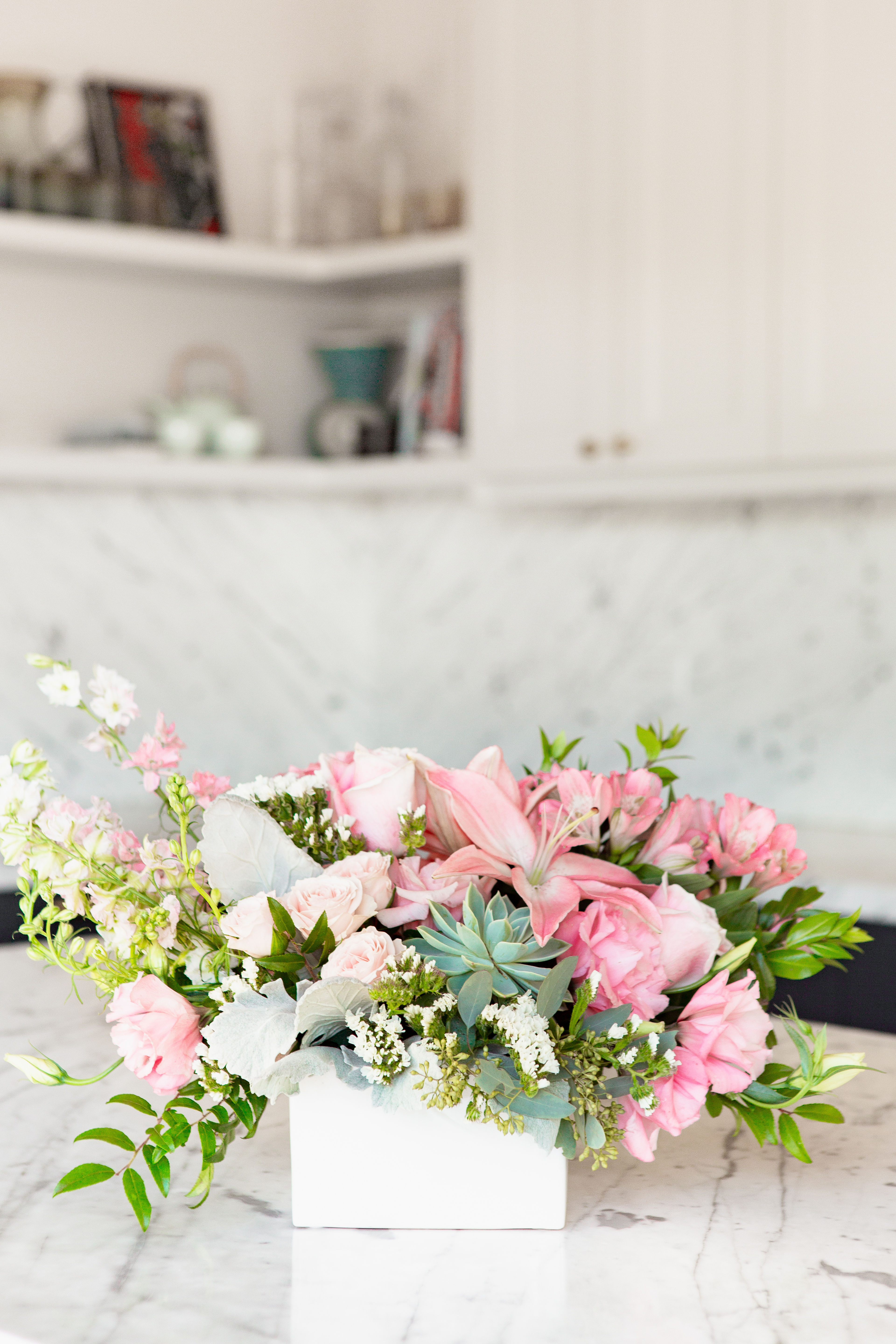 Pink roses, succulents, greenery and more in a white container on a kitchen counter