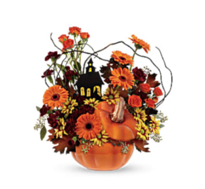 Orange carnations, yellowdaisy spray mums, and more fill a pumpkin vase accented with a haunted ouse cut out 