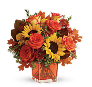 yellow sunflowers, orange roses, gold mums, and more fill an orange cube vase