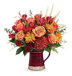 Red alstromeria, maroon carnations, bronze mums, and more fill a maroon ceramic pitcher vase