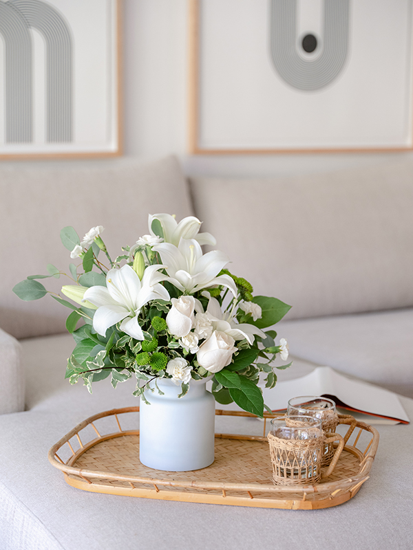 White flowers and greenery in a washed vase on tray table