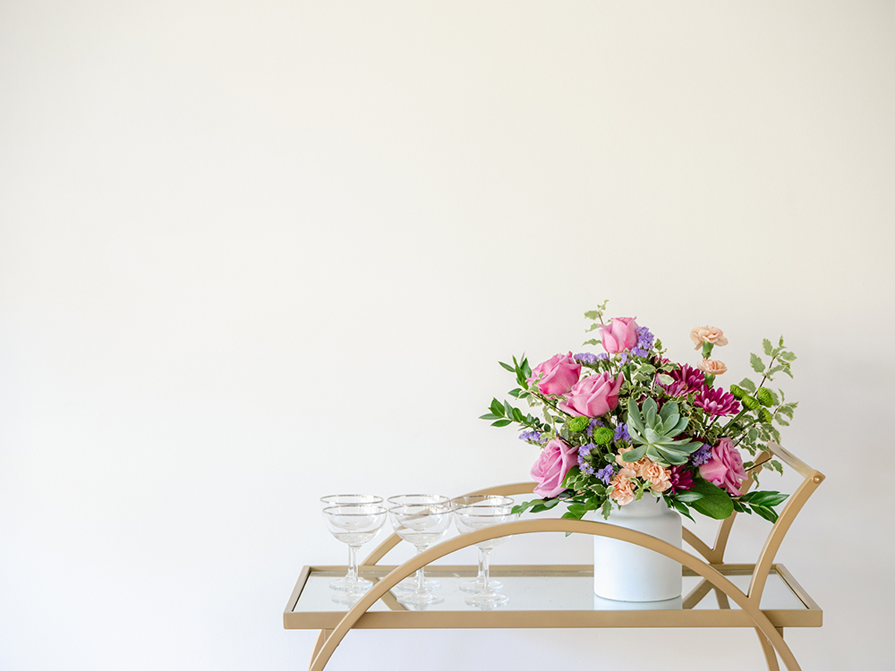 Pink roses, succulents, and more filled a washed vase on bar cart